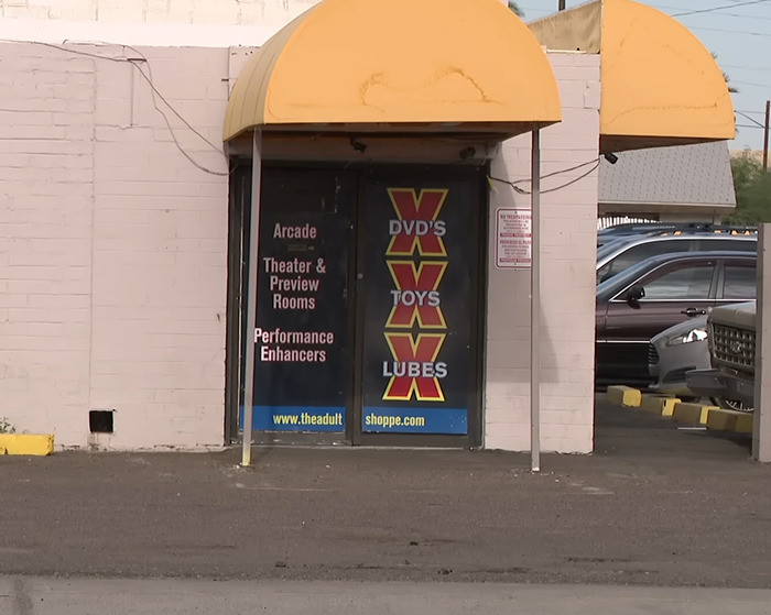 Adult store entrance with signs for DVDs, toys, and lubricants, related to police rescue of kids from hot car incident. - 6