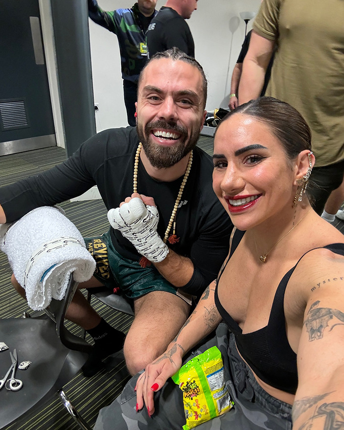 Powerlifter Stefi Cohen smiling with a man wrapped in hand wraps, both seated indoors after training session.