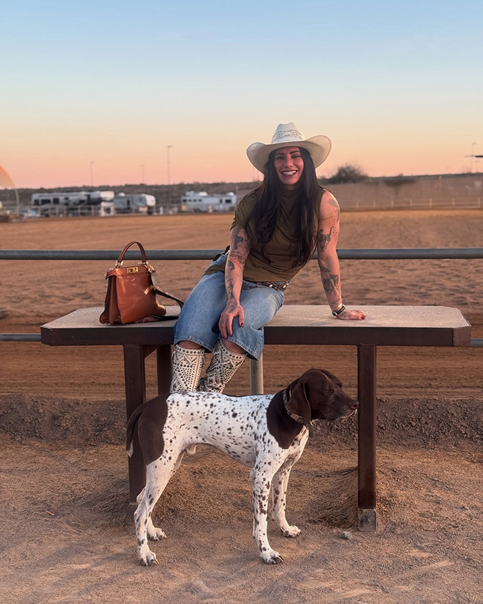 Powerlifter Stefi Cohen sitting outside at sunset with a dog, wearing a cowboy hat and casual outfit.