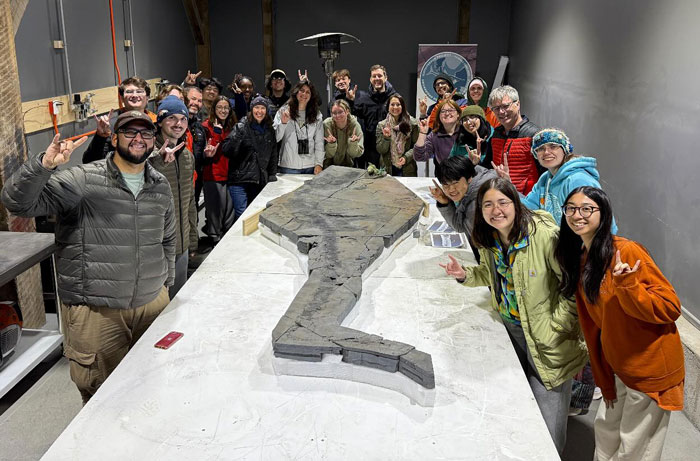 Group of researchers posing with a sea reptile fossil over 100 million years old in a lab setting studying ocean history.