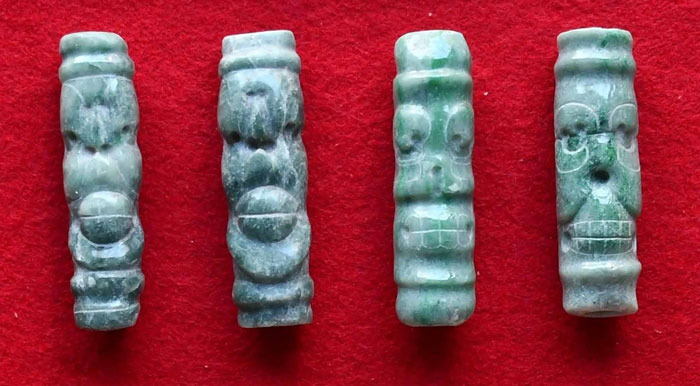 Four small green jade figurines with carved faces displayed on a red background, related to a Maya royal tomb discovery. - 6