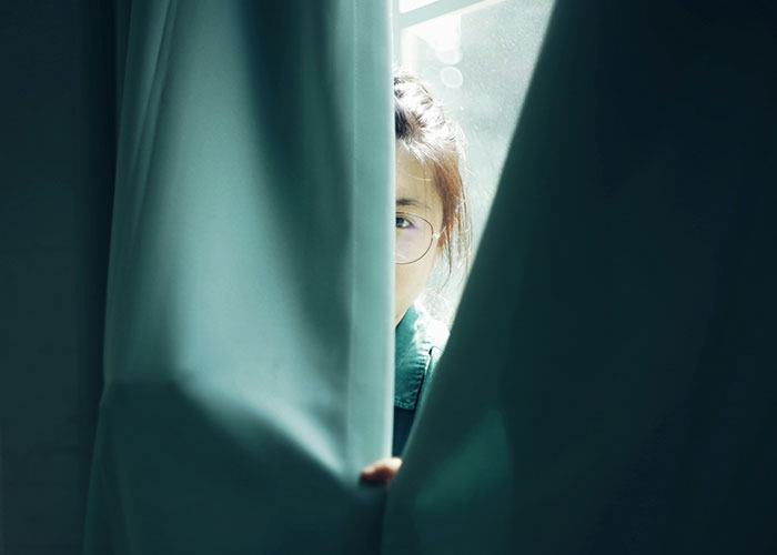 Person wearing glasses peeking through a curtain in natural light, illustrating private investigators discovering strange things. - 5