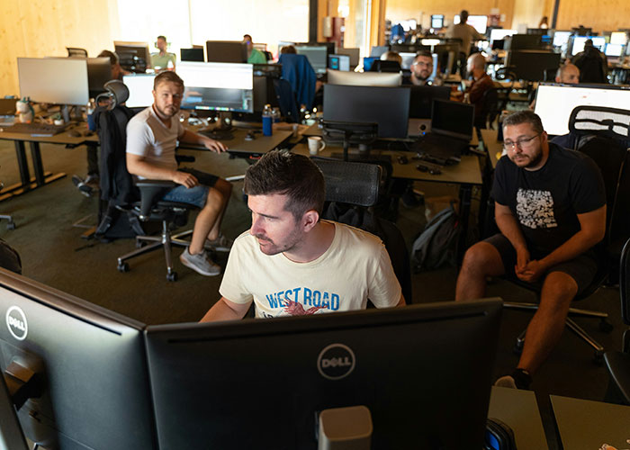 Private investigators working intently in an office with multiple computer monitors and a modern open workspace environment. - 34