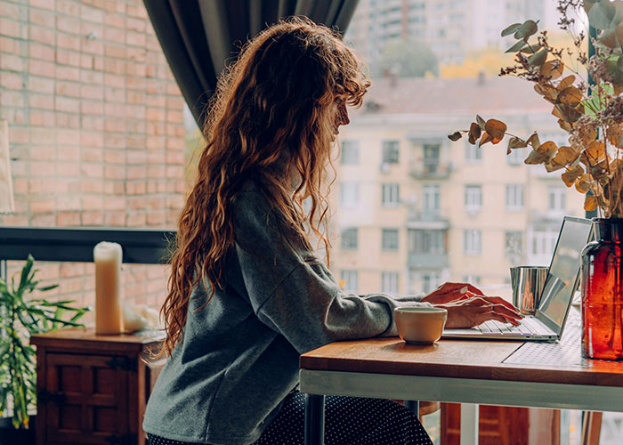 Woman with long curly hair typing on a laptop at a wooden table, researching strange things private investigators discovered. - 4