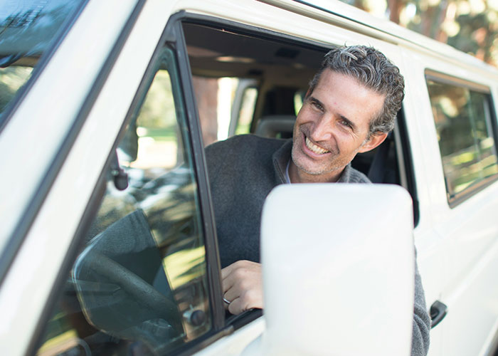 Man smiling inside a white car, representing private investigators discovering strange things during their job. - 20