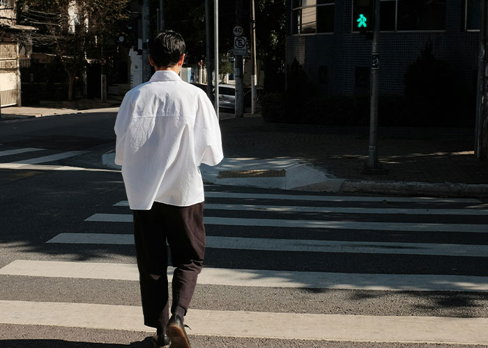 Man in a white shirt and black pants crossing street at a green light, representing strange things private investigators found. - 26
