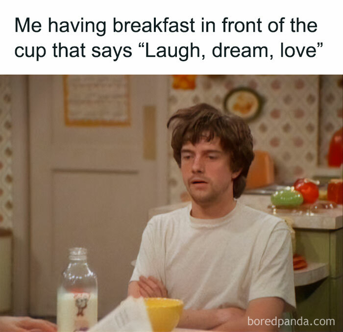 Man having breakfast looking tired with a funny meme about life and a cup that says laugh dream love.