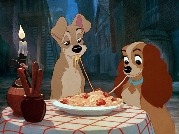 Two animated dogs sharing spaghetti at a table in a romantic scene from a classic Disney movies poll.
