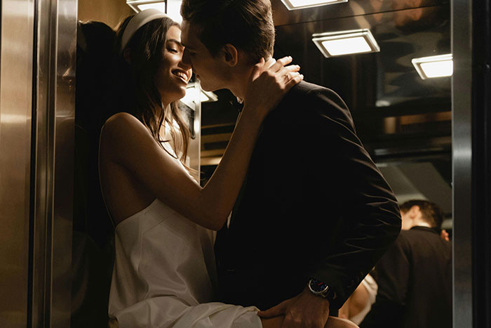 Couple secretly embracing in a dim elevator, illustrating anonymous confessions that could ruin lives if revealed.