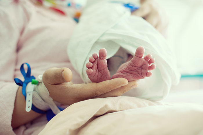 Newborn baby feet resting on a parent's hand with hospital wristbands, depicting intimate anonymous confessions and personal secrets.