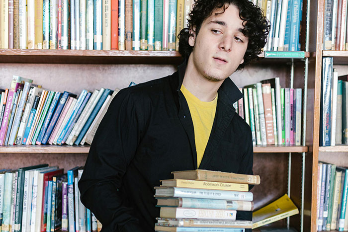 Young man in a library holding a stack of books, captured in a candid moment of anonymous confessions and secrets.