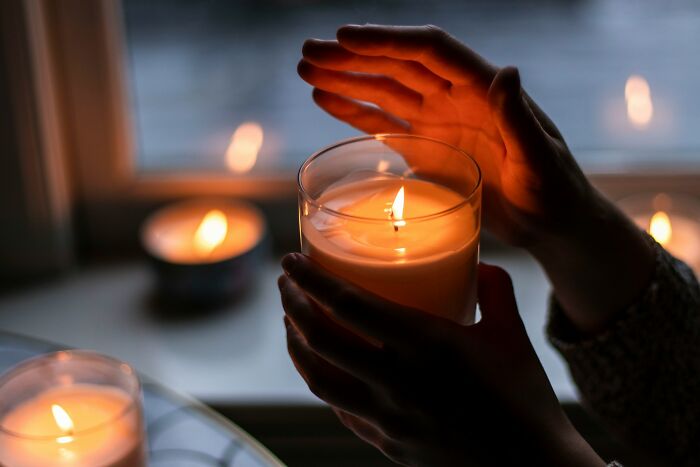 Person warming hands near a lit candle in a dim room, illustrating the concept of smell and sensation.