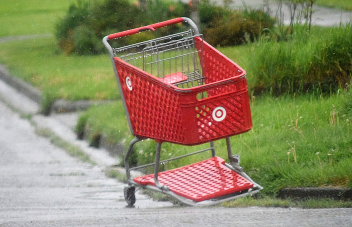 Abandoned red shopping cart on a wet street curb, indicating one of the signs to look out for in unsafe neighborhoods.