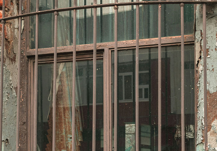 Rusty metal bars on a window with peeling paint on walls, indicating signs of unsafe neighborhoods and areas.