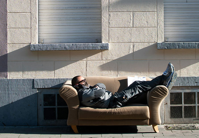 Man wearing mask and sunglasses lying on a couch outdoors, illustrating signs to look out for in unsafe neighborhoods.