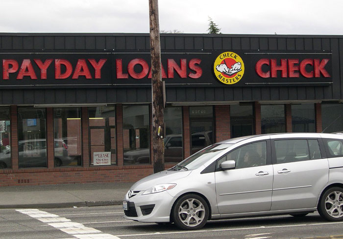Payday loans store on a street with a silver minivan, illustrating signs to look out for in unsafe neighborhoods.