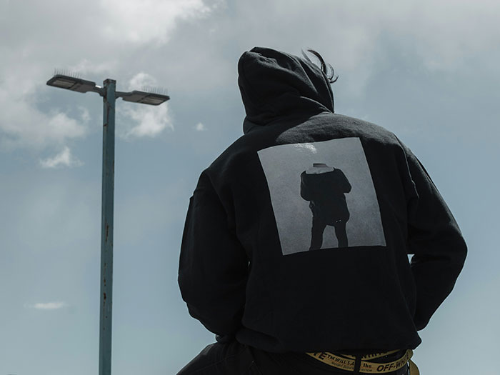 Person in dark hoodie sitting near a streetlight under cloudy sky, illustrating signs to look out for unsafe neighborhoods.