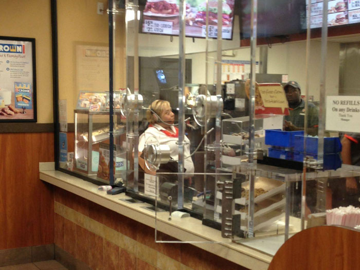 Fast food restaurant counter with employees behind protective screens, highlighting signs to avoid unsafe neighborhoods and areas.