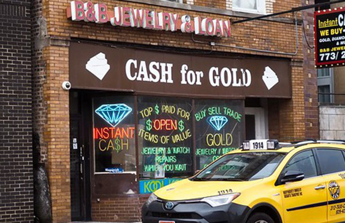 P**n shop storefront with cash for gold signs and a taxi parked outside, illustrating signs of unsafe neighborhoods.