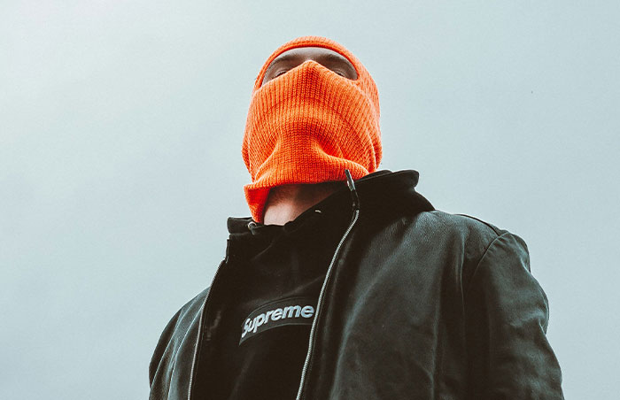 Person wearing an orange balaclava and dark jacket symbolizing signs to look out for in unsafe neighborhoods and areas.