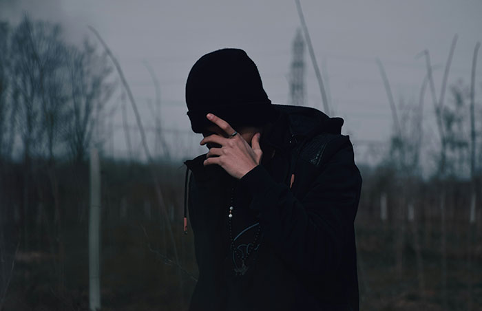 Person wearing dark clothing and a beanie in a gloomy outdoor setting, highlighting signs of unsafe neighborhoods and areas.