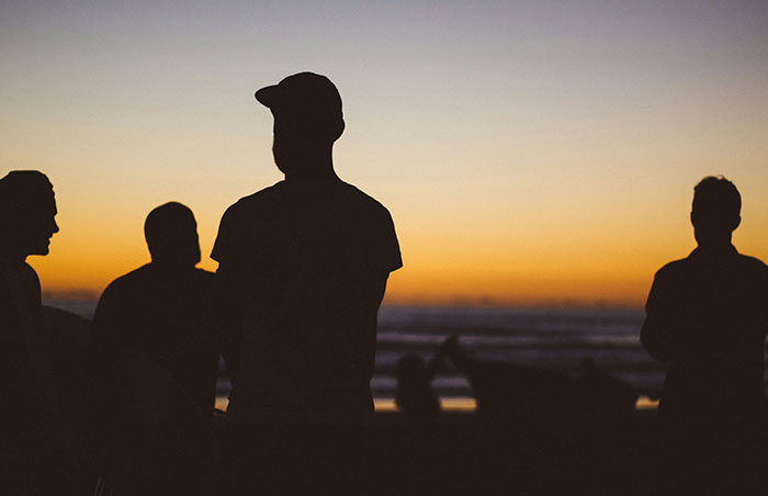 Silhouettes of people gathered at sunset near the beach, highlighting signs to look out for to avoid unsafe neighborhoods.