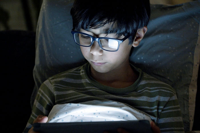 Young boy with glasses using a tablet in dim light, representing concerns around autistic child safety issues. - 4