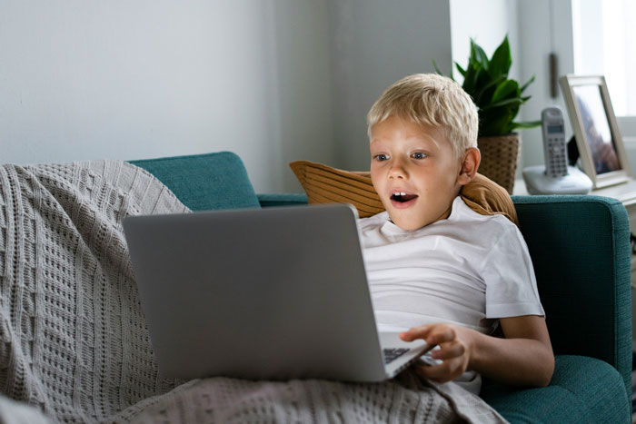 Young boy likely with autism using a laptop on a couch, highlighting concerns about child safety in family settings. - 1