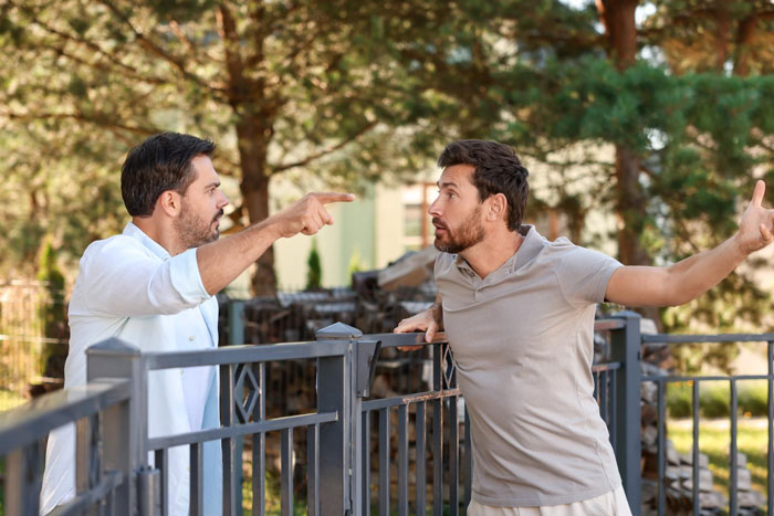 Two men arguing by a fence, illustrating a guy confronting reality about public road parking space in front of his house.