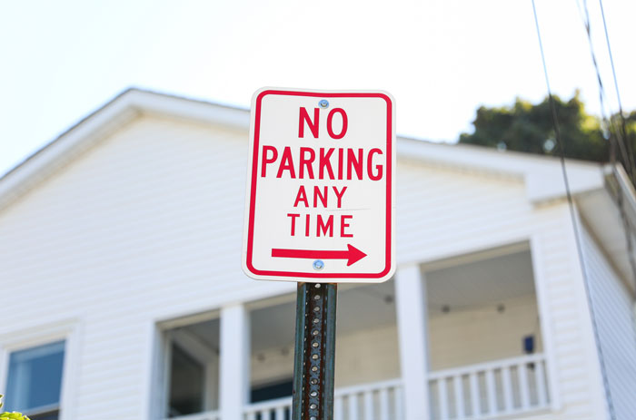 No parking any time sign on a public road in front of a house enforcing parking space rules.