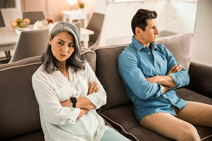 Woman with PhD looks upset sitting opposite her husband on couch with arms crossed in bright modern living room. - 12