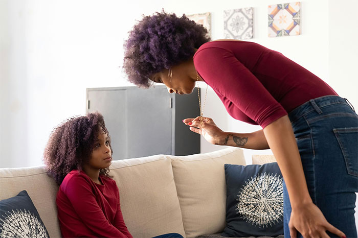 Woman with PhD leaning forward, speaking seriously to a young girl on a couch in a brightly lit living room. - 11