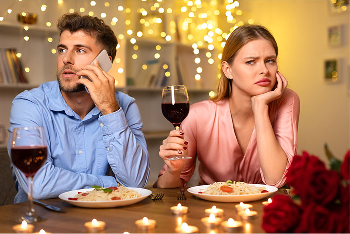 Couple having tense dinner, woman refusing to pay while boyfriend looks upset and distracted on phone. - 1