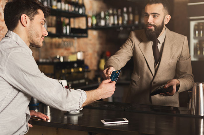 Man handing credit card to bartender at a bar, illustrating a boyfriend refusing to pay in front of friends conflict. - 6