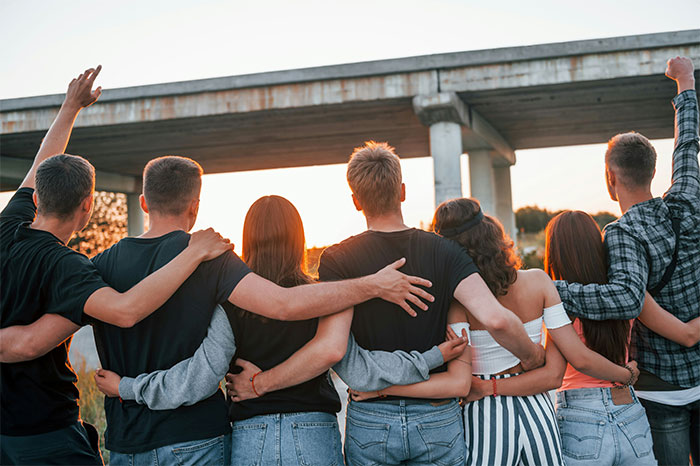 Group of friends with arms around each other standing under a bridge, illustrating boyfriend asking for payment refusal tension. - 10