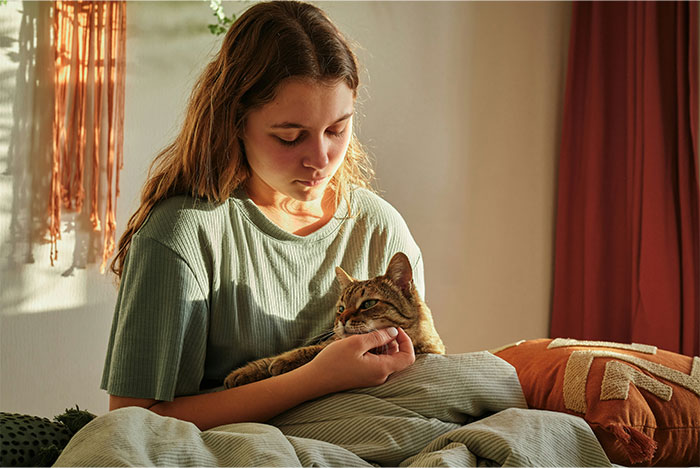Woman sitting on bed holding and looking at her cat, appearing contemplative in a softly lit room - 1
