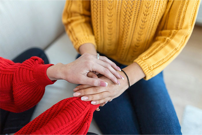 Two women in colorful sweaters holding hands during an emotional conversation about a cat and traumatic childhood. - 49
