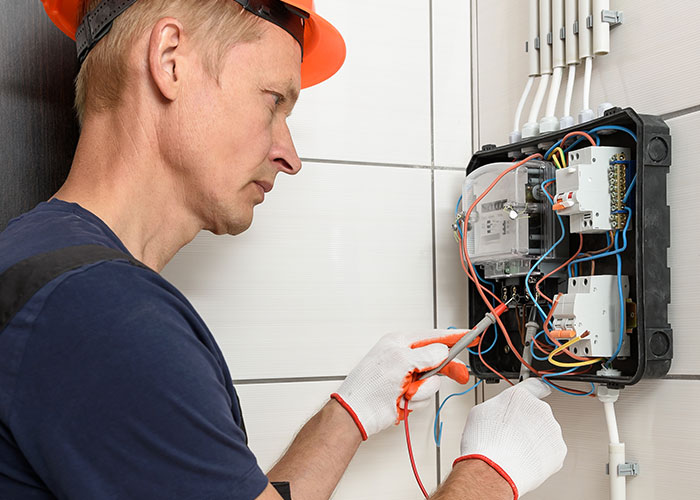 Electrician in safety gloves and helmet working on electrical panel, highlighting seemingly harmless things that are very dangerous.