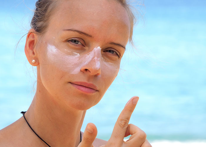 Woman applying sunscreen on her face at the beach, highlighting seemingly harmless things that can be very dangerous.