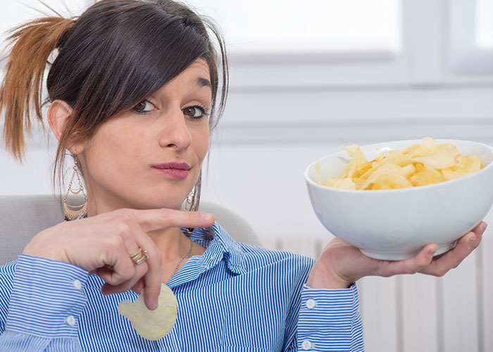 Woman holding a bowl of potato chips, highlighting seemingly harmless things that can be actually very dangerous.