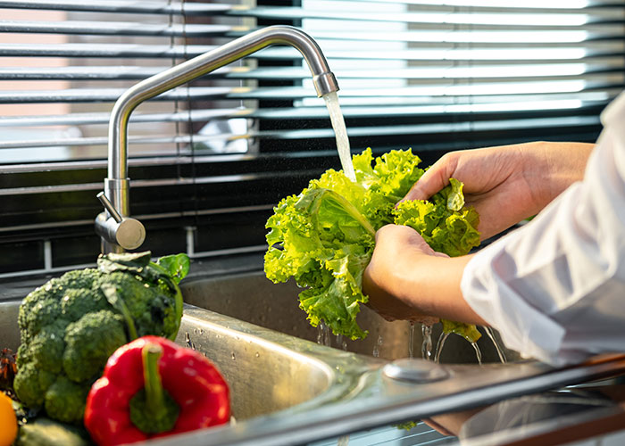 Washing fresh lettuce under running water in kitchen sink, illustrating seemingly harmless things that are actually very dangerous.