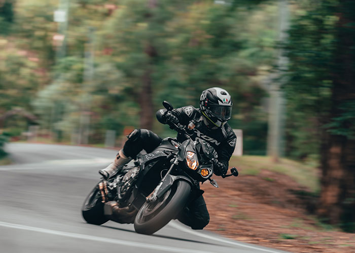 Motorcyclist wearing protective gear riding a black sportbike on a winding road, highlighting seemingly harmless dangers.