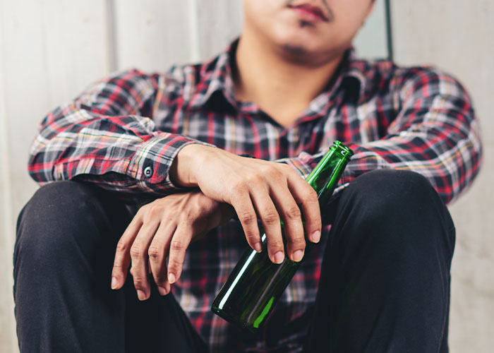 Young man sitting on the floor holding a green bottle, representing seemingly harmless things that are actually very dangerous