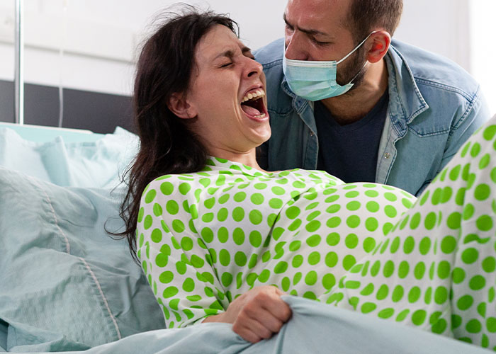 Woman in labor experiencing pain in hospital bed with a masked man supporting her, showing seemingly harmless things that can be dangerous.