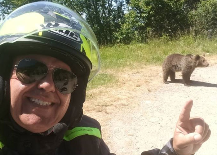 Man in helmet and sunglasses pointing at a bear on a sunny dirt path, showing seemingly harmless things that are dangerous.