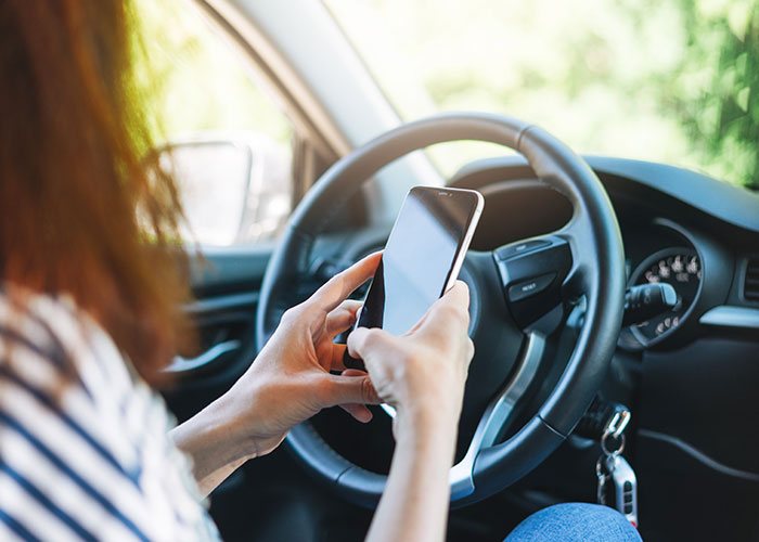 Person texting on a smartphone while driving a car, illustrating seemingly harmless things that are actually very dangerous.
