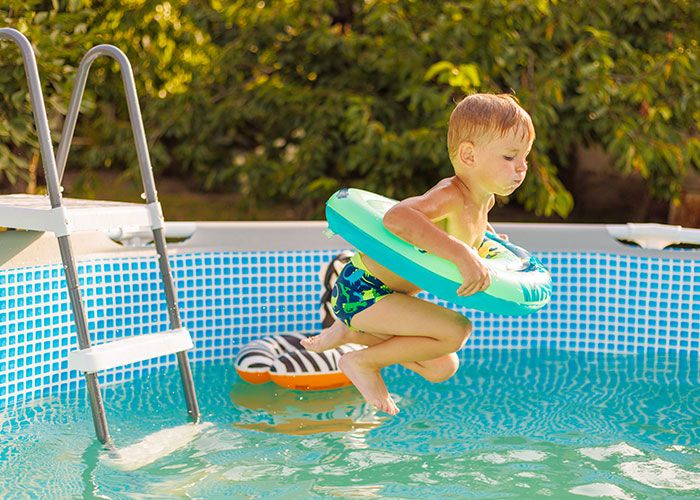 Young boy jumping into pool with float ring playing outdoors, illustrating seemingly harmless things that are dangerous risks.