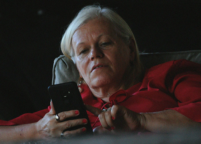 Older woman in red shirt struggling with smartphone, representing a boss bad with technology trying to spy on coworker.