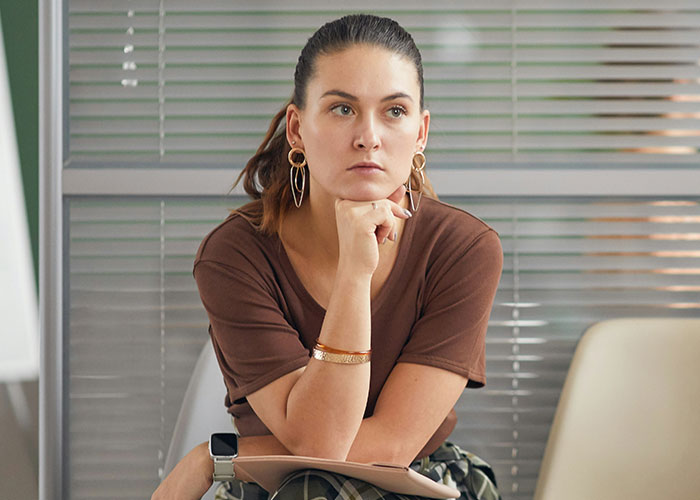 Woman boss struggling with technology, looking thoughtful in a modern office setting, holding a tablet with concern.