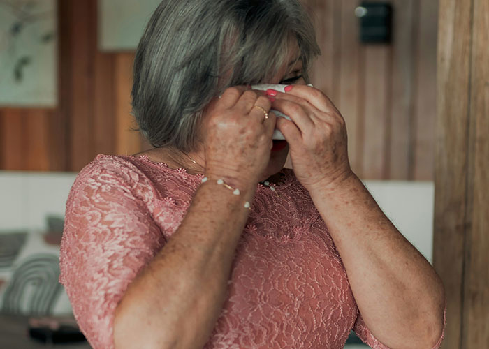 Middle-aged woman in pink lace dress wiping tears, depicting a boss struggling with technology and emotional stress.
